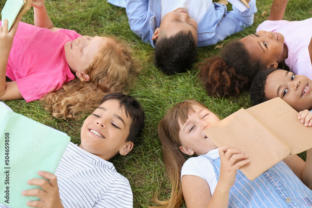 Poster Little children with books lying on green grass in park