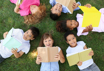 Little children with books lying on green grass in park
