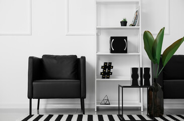 Stylish interior of room with armchairs, shelf unit, modern speakers and vase with palm leaves