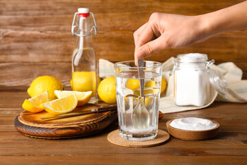 Woman mixing water with baking soda on wooden background