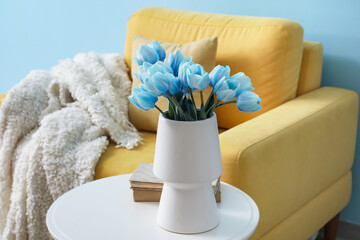 Vase with blue tulips and books on table in living room