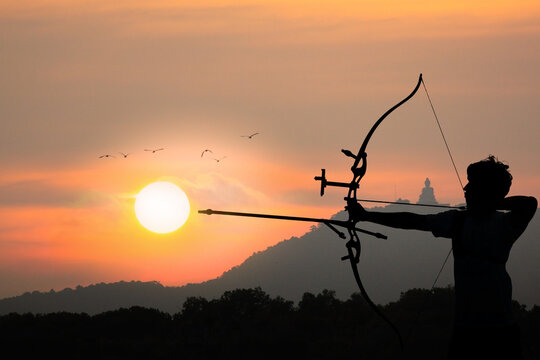 Silhouette of a man with  weapon bow and arrow on a background of sky and sunset