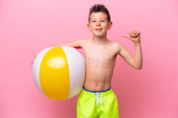 Little caucasian boy holding a beach ball isolated on pink background proud and self-satisfied