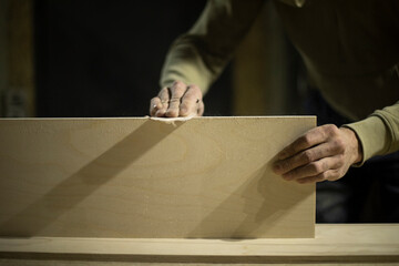 Carpenter grinds board. Man creates furniture. Hands hold sanding paper.