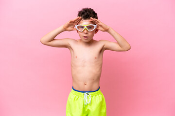 Little caucasian boy wearing a diving goggles isolated on pink background with surprise expression