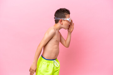 Little caucasian boy wearing a diving goggles isolated on pink background shouting with mouth wide open to the side © luismolinero