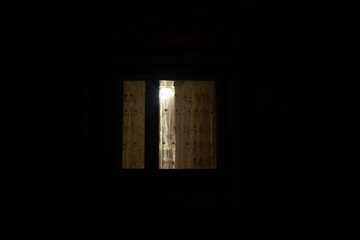 Window is in dark. Curtains on window at night.