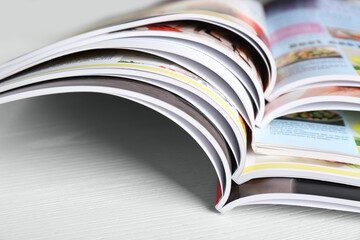 Many open magazines on white wooden table, closeup