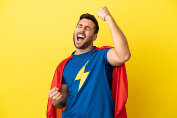Young handsome caucasian man isolated on yellow background in superhero costume and celebrating a...