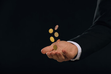 Man and coins falling into his hand on black background, closeup