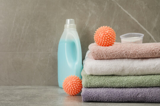 Dryer balls, detergents and stacked clean towels on grey marble table. Space for text