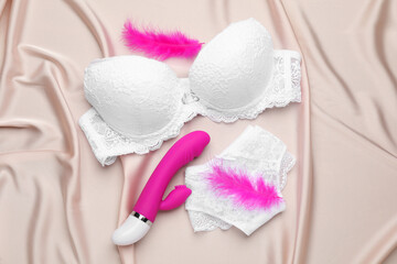 Vibrator, feathers and lingerie on beige silky fabric, flat lay