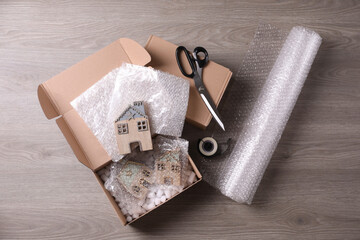 Open box with decorative house figures, adhesive tape, scissors, foam peanuts and bubble wrap on...