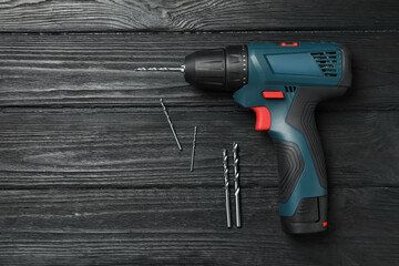 Modern electric power drill and different bits on black wooden table, flat lay. Space for text