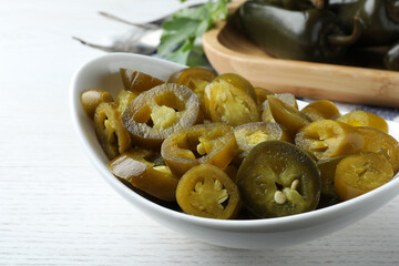 Bowl with slices of pickled green jalapeno peppers on white wooden table, closeup