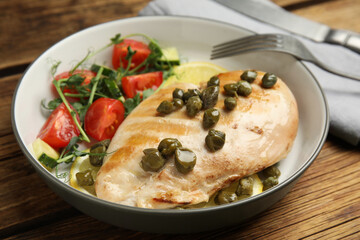 Delicious cooked chicken fillet with capers and salad served on wooden table, closeup