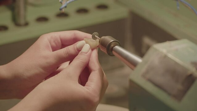 Close up of woman's hands carving a piece of jade using stone carving machine.