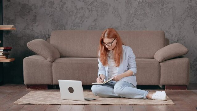 woman with red hair using laptop sitting on the floor in living room in apartment working at home