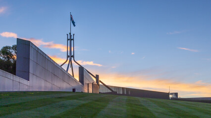 Australian Parliament House Canberra Australian Capital Territory. Showing the grassed roof at sunset and the Australian Flag - obrazy, fototapety, plakaty