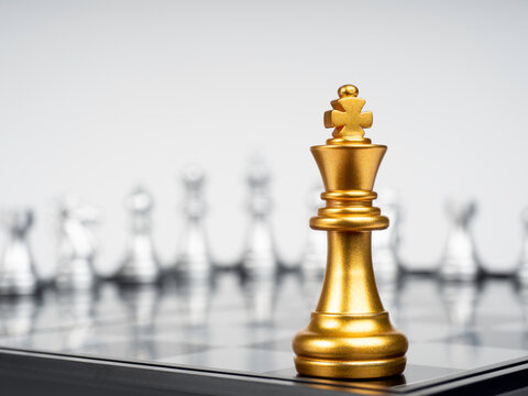 The Golden king chess piece standing on chessboard corner in front of many silver chess pieces on white background. Leadership, fighter, competition, confrontation, and business strategy concept.