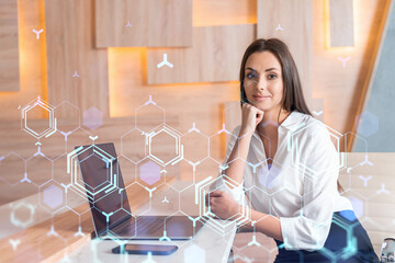 Attractive businesswoman in white shirt at workplace working with laptop to optimize development by implying new technologies in business process. Hi tech hologram over office background