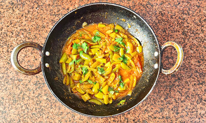 Parwal curry (Pointed gourd curry) in black wok on brown background