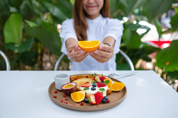 Closeup image  of a young woman holding and showing a piece of an orange while eating mixed fruits...
