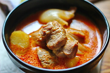 Massaman curry in black crockery served with boiled potatoes and chili on a brown wooden table.
