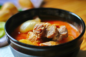 Massaman curry in black crockery served with boiled potatoes and chili on a brown wooden table.