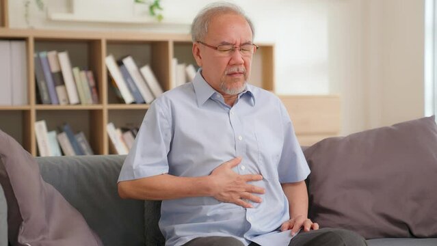 Asian senior elderly terrible pain stomach ache on couch. Stressed older man suffering from abdominal pain touching on abdomen, appendicitis sit on sofa. Healthcare medical insurance. food poisoning.