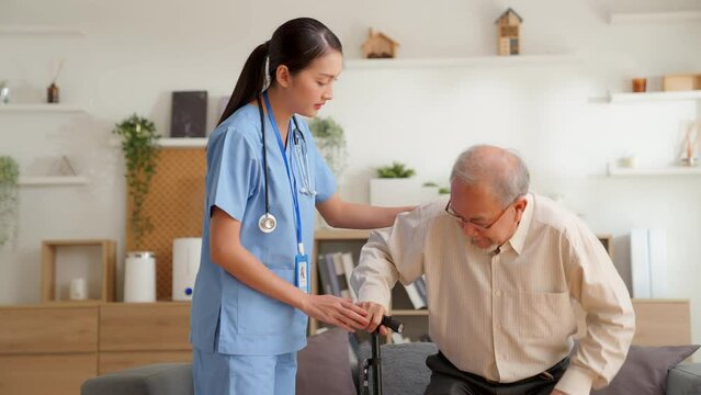 Asian young woman nurse helping senior elderly man physical therapy walk with crutches at home. Physiotherapist, Rehabilitation Doctor, Assist Disabled Patients. older people healthcare concept