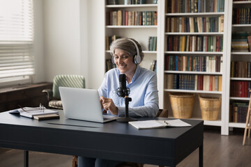 Happy older grey haired business blogger woman making video call on laptop, using laptop, wireless...