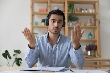 Serious handsome freelance employee man in headphones head shot portrait. Positive engaged blogger, online teacher, coach talking on video conference call, speaking, looking at camera