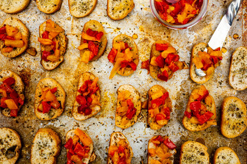 bruschetta mini toasts spread with oily gourmet red, yellow, and orange pepper topping on baking sheet  - 504691661