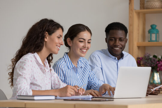 Diverse group of happy interns and mentor talking at laptop computer, discussing new professional skills, watching online learning presentation, smiling, laughing. Business education, internship