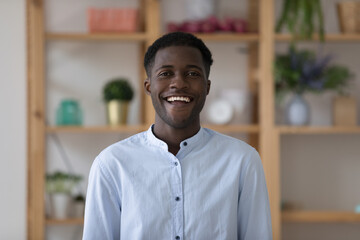 Happy millennial African American intern, entrepreneur, freelance employee head shot business portrait. Young Black professional man, leader posing indoors, looking at camera with toothy smile