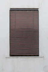 window with shutters, brown jalousie rolled up, grey cement wall, no person