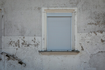 very old window jalousie closed, shutter rolled up,  house facade with shabby and cracked wall