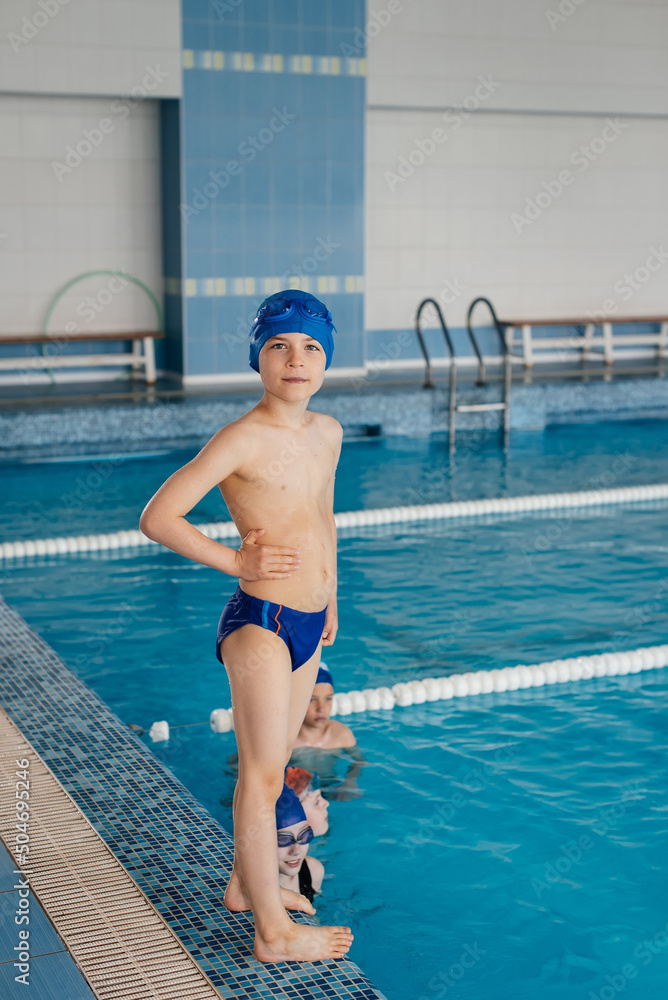 Wall mural A group of boys and girls play and learn to swim in a modern swimming pool. Development of children's sports. Healthy parenting and promotion of children's sports.