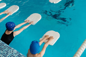 A group of boys and girls train and learn to swim in a modern swimming pool with an instructor. Development of children's sports. Healthy parenting and promotion of children's sports.
