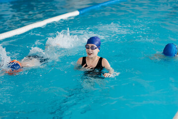 A group of boys and girls play and learn to swim in a modern swimming pool. Development of children's sports. Healthy parenting and promotion of children's sports.