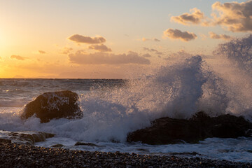 Sea ​​wave at sunset hitting  rock on the beach.