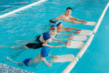 A group of boys and girls train and learn to swim in a modern swimming pool with an instructor. Development of children's sports. Healthy parenting and promotion of children's sports.