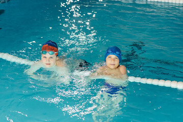 A group of boys play and learn to swim in a modern swimming pool. Development of children's sports. Healthy parenting and promotion of children's sports.