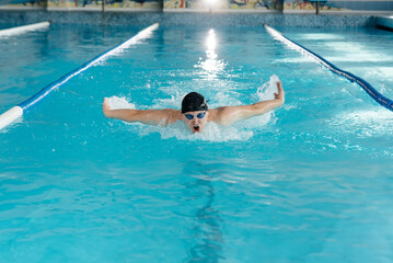 A young man trains and swims in a modern swimming pool. Sports development. Preparation for...