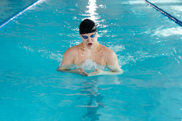 A young man trains and swims in a modern swimming pool. Sports development. Preparation for...