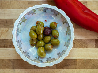 decroative bone china dish containing green and black olives with a red chilli dressing