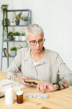 Serious Middle-aged Businesswoman In Eyeglasses Checking Time On Watch While Scheduling Supplements Intake, Nutritional Genomics Concept