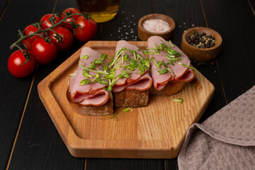 Toast on fresh toasted bread with cream cheese, ham and microgreens, on a wooden hexagonal plate, open space