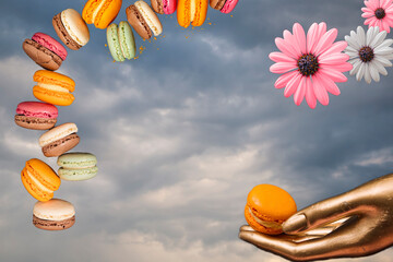 Composition - Summer margarita flower, golden female hand holding golden macaroni and macarons floating on the background of a summer cloudy day.